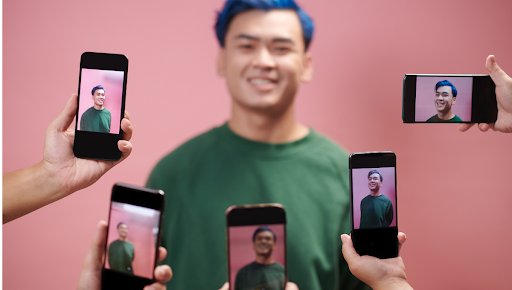 Influenceur posant devant un fond rose pendant une séance photo, entouré de plusieurs smartphones capturant son image pour une campagne de marketing d'influence
