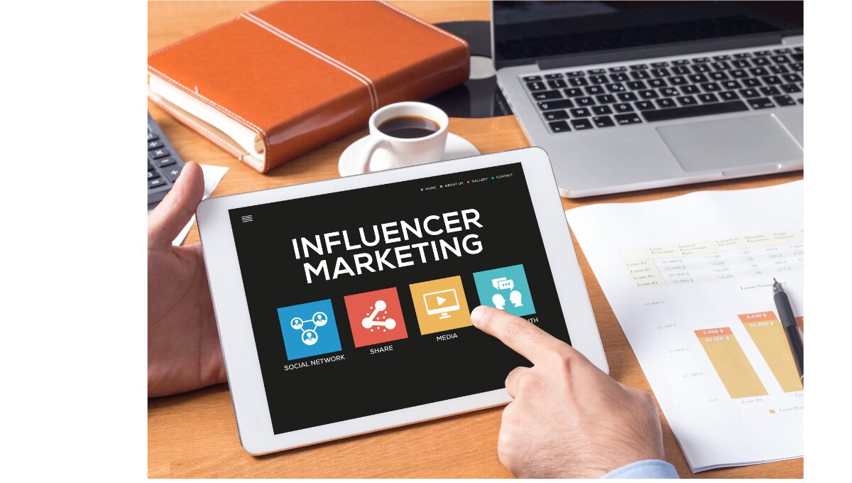 Personne consultant une tablette affichant les options d'une plateforme de marketing d'influence, avec des icônes représentant les réseaux sociaux, le partage, les médias et la croissance, dans un environnement de travail professionnel.